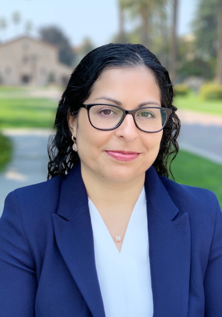 Head shot of Hooria Jazaieri, a light-skinned woman with curly black hair wearing glasses and a blue jacket.